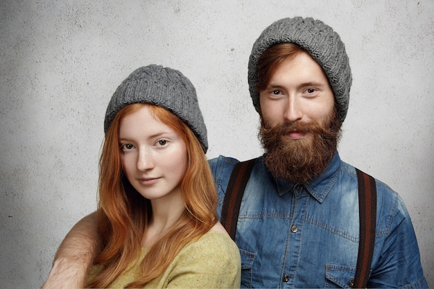 Pretty woman with long red hair and handsome man dressed in winter clothes standing isolated against wall 