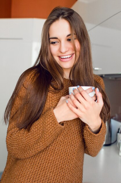 日当たりの良い秋の朝の時間にモダンなキッチンでお茶の白いカップのきれいな女性。