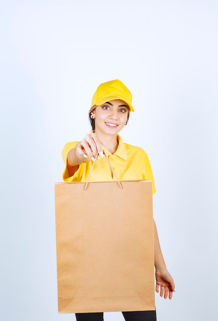 A pretty woman in yellow uniform holding brown blank craft paper bag . 