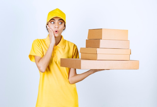 A pretty woman in yellow uniform holding brown blank craft paper boxes. 