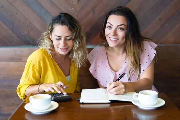 Pretty women drinking coffee and using calculator in cafe