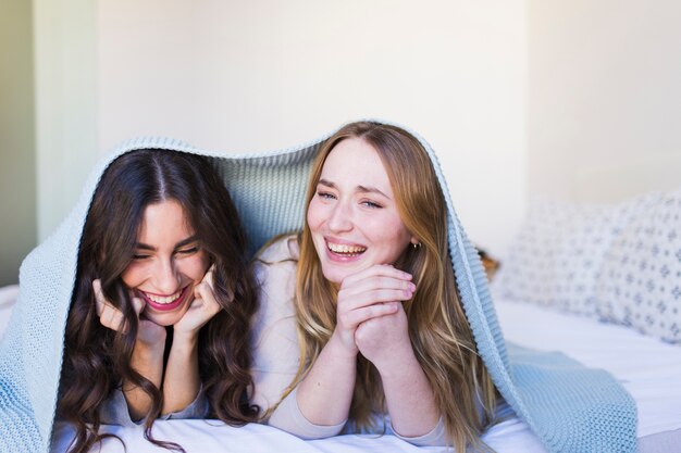 Pretty women laughing under blanket