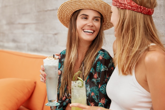 pretty women recreate together at coffee shop, drink fresh cocktails . Relaxed adorable females relax during summer holidays.