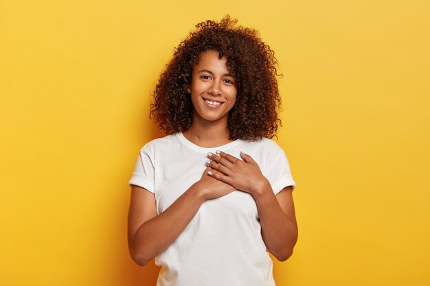 Симпатичная молодая афроамериканка держит ладони у сердца и выражает благодарность