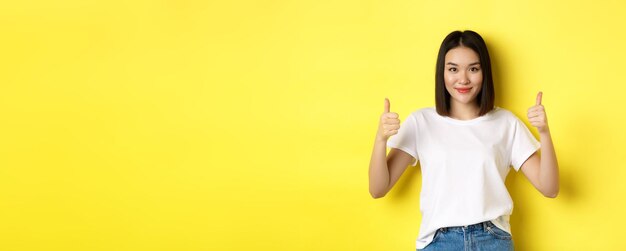 Foto gratuita la donna asiatica abbastanza giovane in maglietta bianca che mostra i pollici in su e che sorride elogia la buona offerta raccomanda p