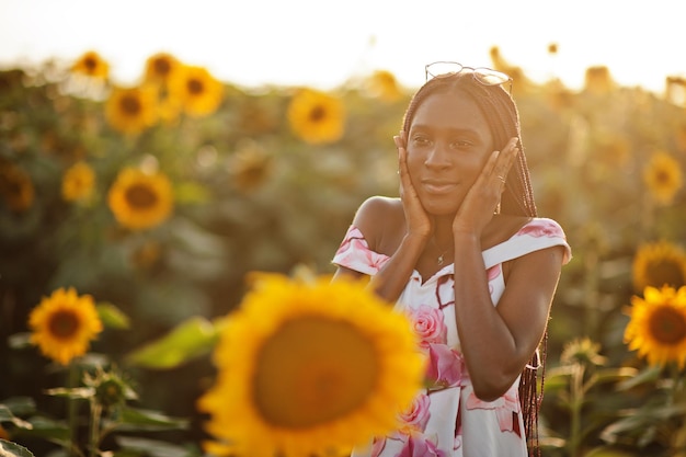 Piuttosto giovane donna nera indossare abito estivo posa in un campo di girasoli