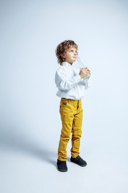 Pretty young boy in casual clothes on white  wall. Fashionable posing. Caucasian male preschooler with bright facial emotions. Childhood, expression, having fun. Drinking milk, enjoying,