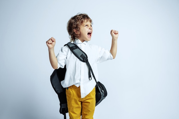 Foto gratuita ragazzo abbastanza giovane in abiti casual sul muro bianco. posa alla moda. bambino in età prescolare maschio caucasico con emozioni facciali luminose. infanzia, divertimento. emozioni espressive, urla.