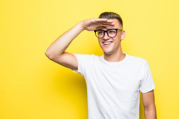 Pretty young boy looks forward dressed up in white t-shirt and transperent glasses isolated on yellow