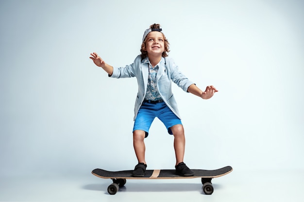 Pretty young boy on skateboard in casual clothes on white