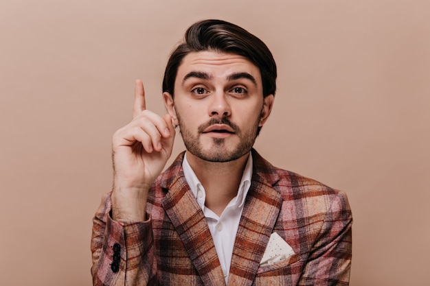 Free photo pretty young brunette-haired boy looking straight forward and pointing one finger, while having idea