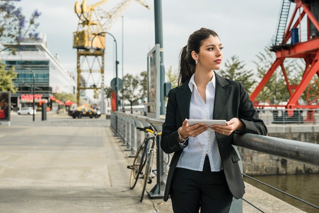 Free photo pretty young businesswoman standing on street holding mobile in hand