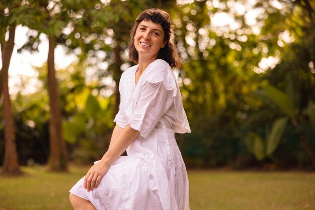 Pretty young caucasian brunette woman wear white sundress looks at camera spending time outdoors in summer