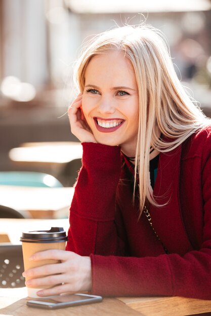 Pretty young caucasian lady sitting in cafe outdoors drinking coffee