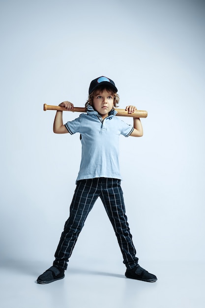 Pretty young curly boy in casual clothes on white wall. Confident and cool with sport bat. Caucasian male preschooler with bright facial emotions. Childhood, expression, having fun.