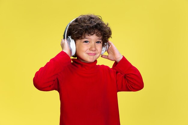 Pretty young curly boy in red wear on yellow studio background. Childhood, expression, fun.