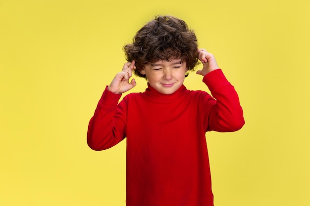 Pretty young curly boy in red wear on yellow studio background. childhood, expression, fun.