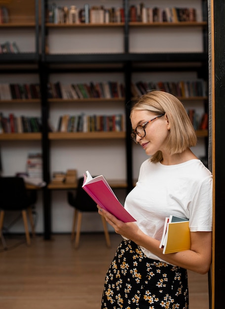 Довольно молодая девушка, читающая книгу в библиотеке