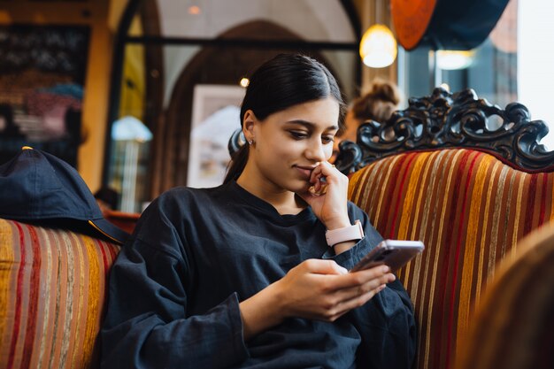 カフェの大きな柔らかい椅子で休んで、電話でチャット、時間をチャットのかなり若い女の子