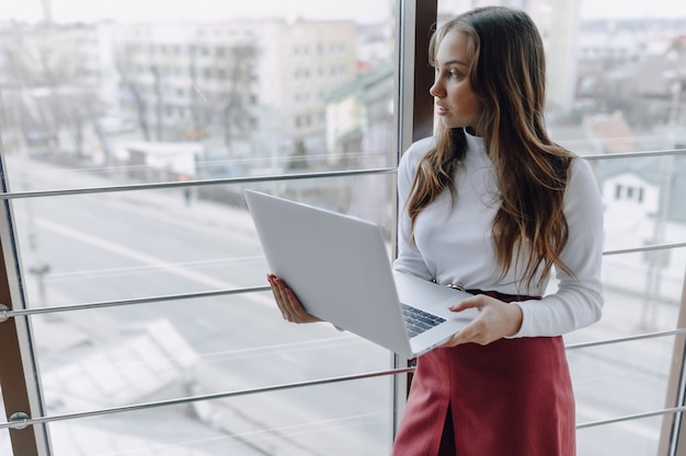 Pretty young girl with laptop by the window