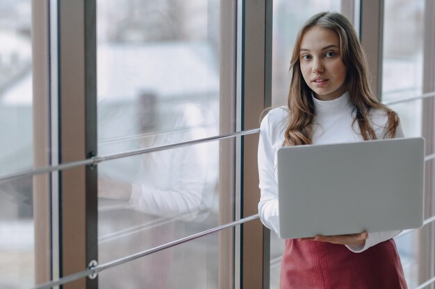 Ragazza graziosa con un computer portatile dalla finestra