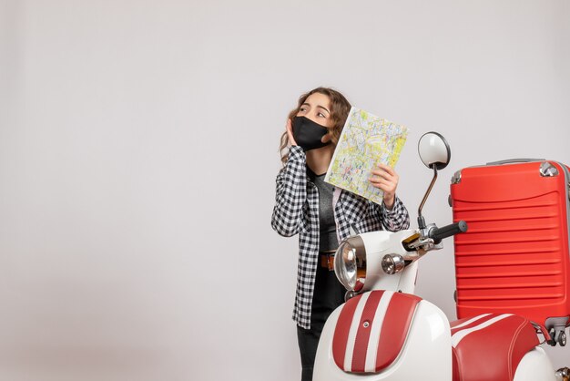 pretty young girl with mask holding map standing near moped with suitcase