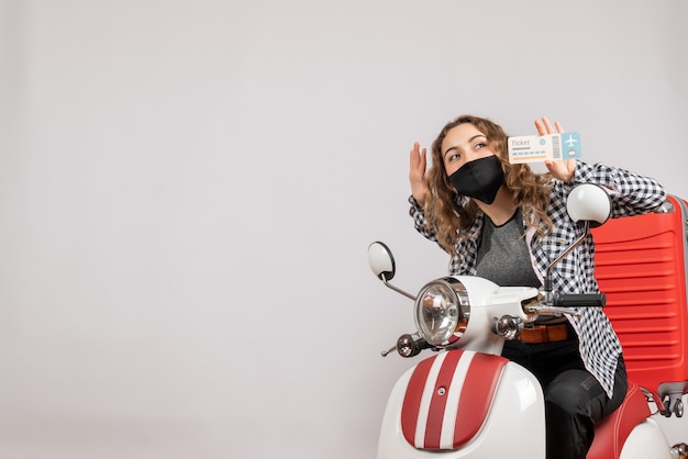 pretty young girl with mask on moped holding up travel ticket