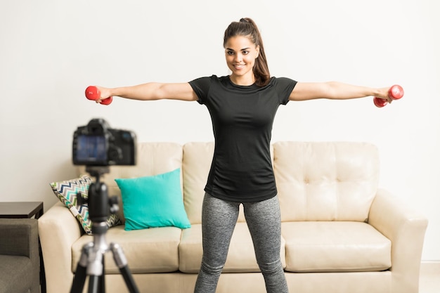 Pretty young Hispanic fitness blogger exercising on camera and giving some advice