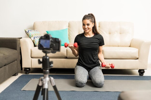 Pretty young Hispanic fitness blogger working out on camera and giving some advice to her followers