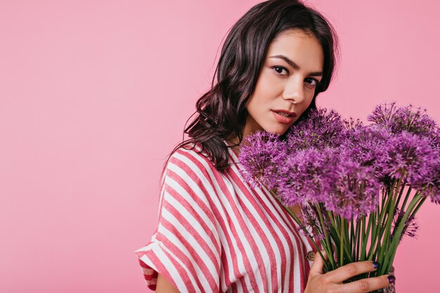 Pretty young lady looks mysteriously. Girl in striped top enjoying colorful bouquet.