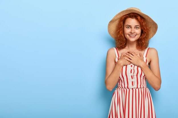 Pretty young lady with ginger hair posing in summer dress and straw hat