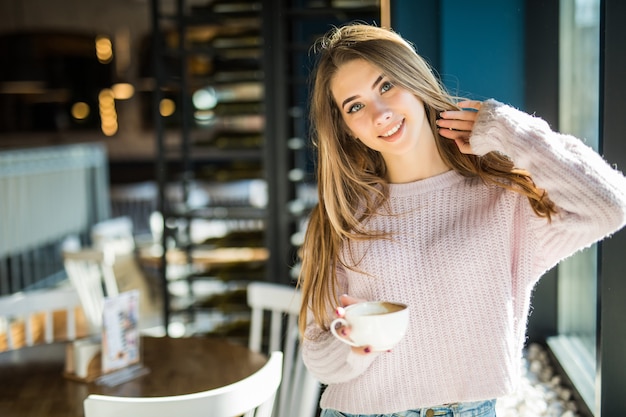 카페에서 캐주얼 옷 청바지를 입고 꽤 젊은 모델 학생 십 대 아가씨는 그녀의 손에 커피 차 잔을 보유