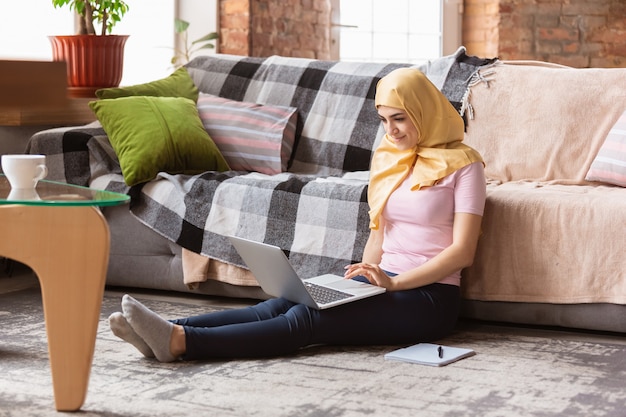 かなり若いイスラム教徒の女性が自宅で検疫と自己絶縁中にタブレットを使用してselfieまたはビデオ通話、オンラインレッスン