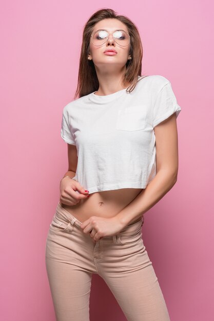 Pretty young sexy fashion sensual woman posing on pink background dressed in hipster style jeans