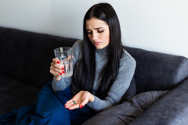 錠剤と水のガラスを自宅で朝を保持しているかなり若い病気の女性