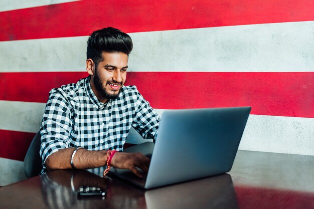 Pretty, young , smiling African man in formalwear using his laptop while leaning at bar.