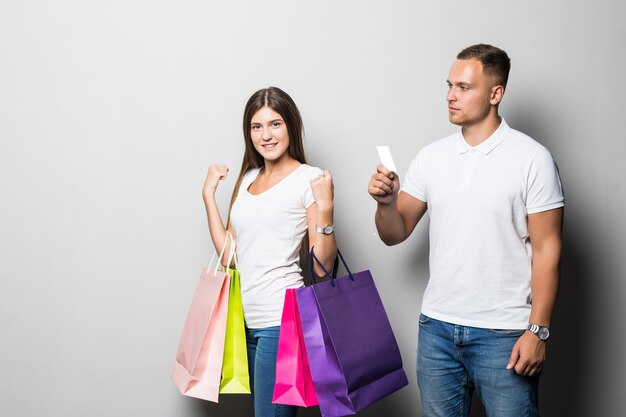 Pretty young smiling sunny student couple holding a lot of coloured shopping bags isolated on white background