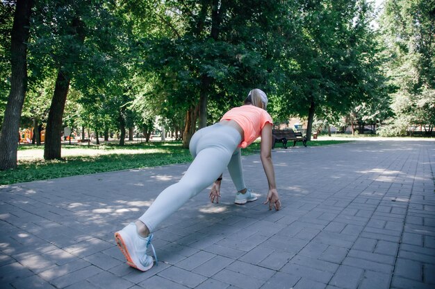 Pretty young sporty woman in park in sportswear warming up exercising stretching getting ready for s...