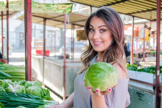 Pretty young woman buying vegetables on the market. young woman holding cabbage in hand on marketplace.  Women  holding fresh green ripe cabbage