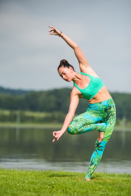 Pretty young woman doing yoga exercises in the park