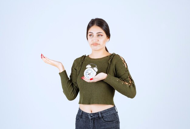 Pretty young woman holding alarm clock with enreadable expression.