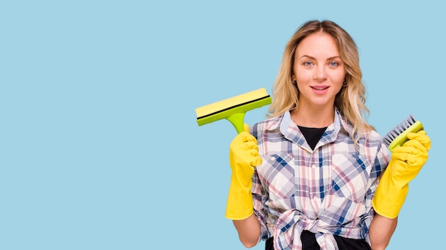 Pretty young woman holding cleaning supplies against blue background