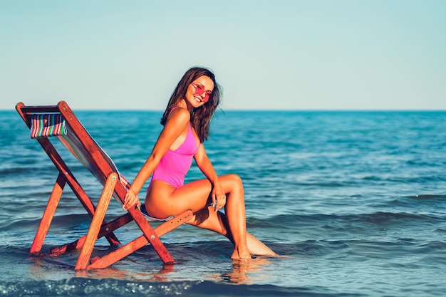 ラウンジャー​の​ビーチ​で​リラックスした​ピンク​の​ビキニ​の​かなり​若い​女性​夏休み​の​コンセプト