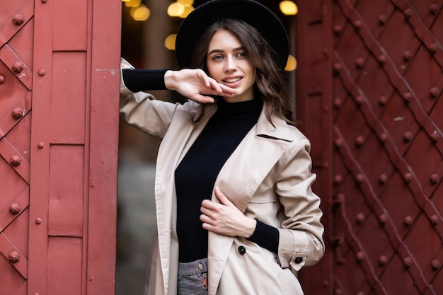 Pretty young woman near old fashion door wearing black hat and coat on the street.