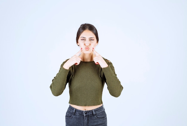 Foto gratuita donna abbastanza giovane che pizzica le sue guance sulla parete bianca