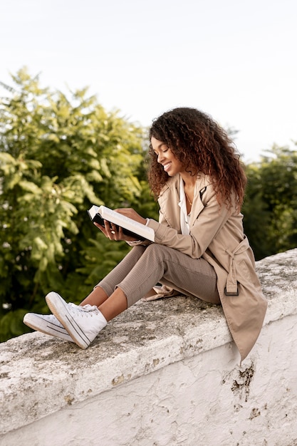 Pretty young woman reading a book outdoors