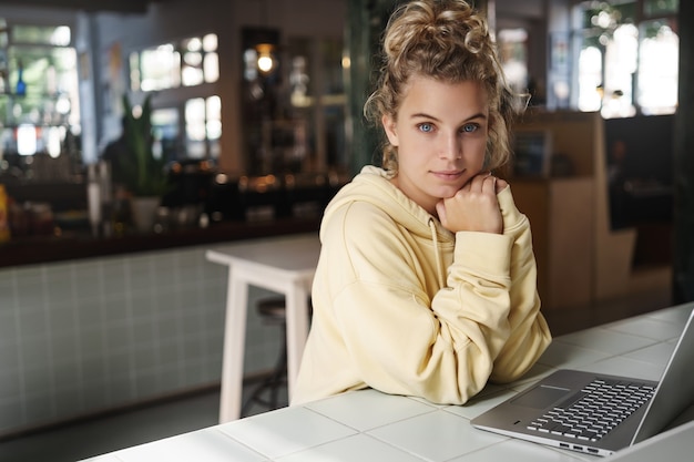 Pretty young woman sits alone in a cafe with a laptop computer.