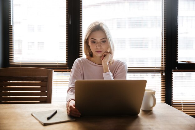 Free photo pretty young woman sitting near coffee while work with laptop