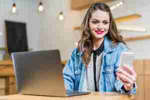 Foto gratuita giovane donna graziosa che si siede nel ristorante che esamina telefono cellulare