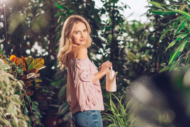 Pretty young woman standing in the garden holding small watering can